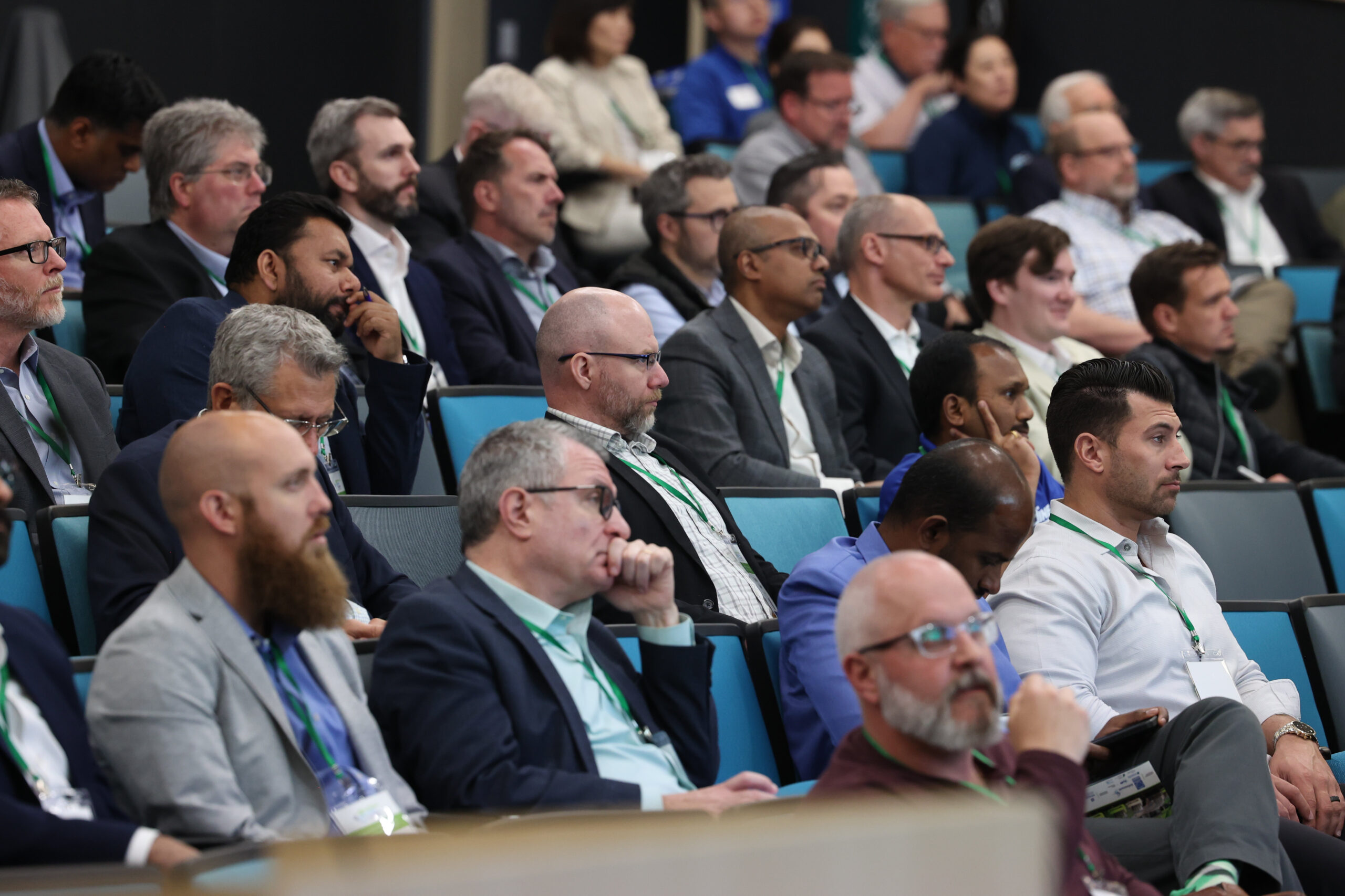 A large audience of professionals attentively listening during a H2EA-NA conference session in a lecture hall; most attendees wear business attire and green lanyards. This photo was taken at the North American Hydrogen Engine Conference.